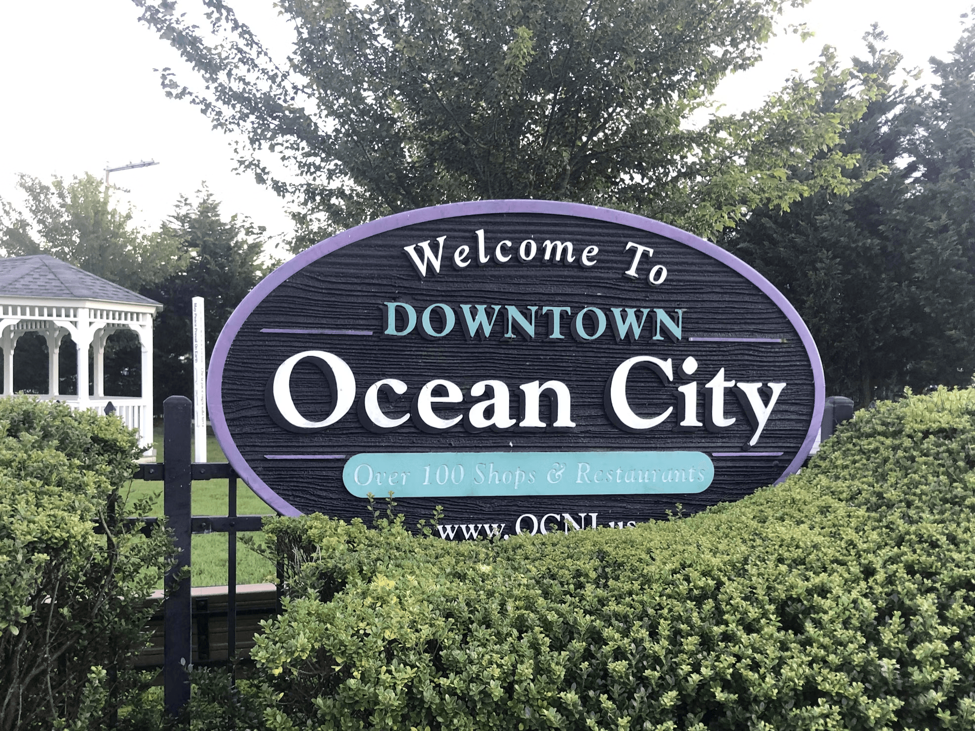 The Welcome to Downtown Ocean City sign behind green hedges.